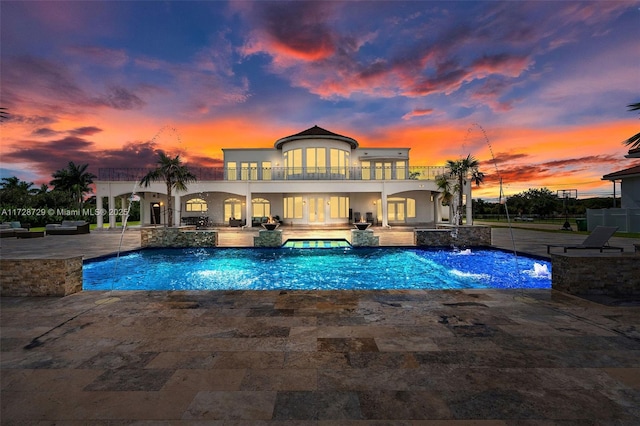 pool at dusk featuring pool water feature, a patio area, and an in ground hot tub