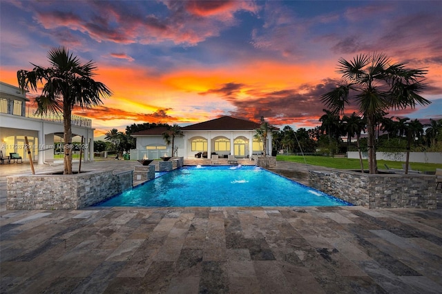 pool at dusk with pool water feature and a patio area