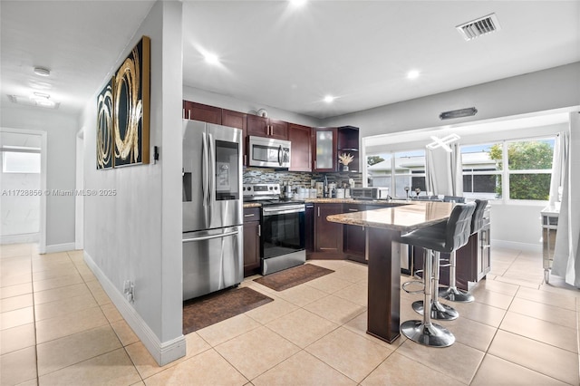 kitchen featuring a breakfast bar, decorative backsplash, stainless steel appliances, light tile patterned floors, and light stone counters