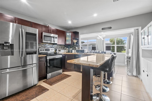 kitchen featuring tasteful backsplash, light stone countertops, appliances with stainless steel finishes, and light tile patterned flooring