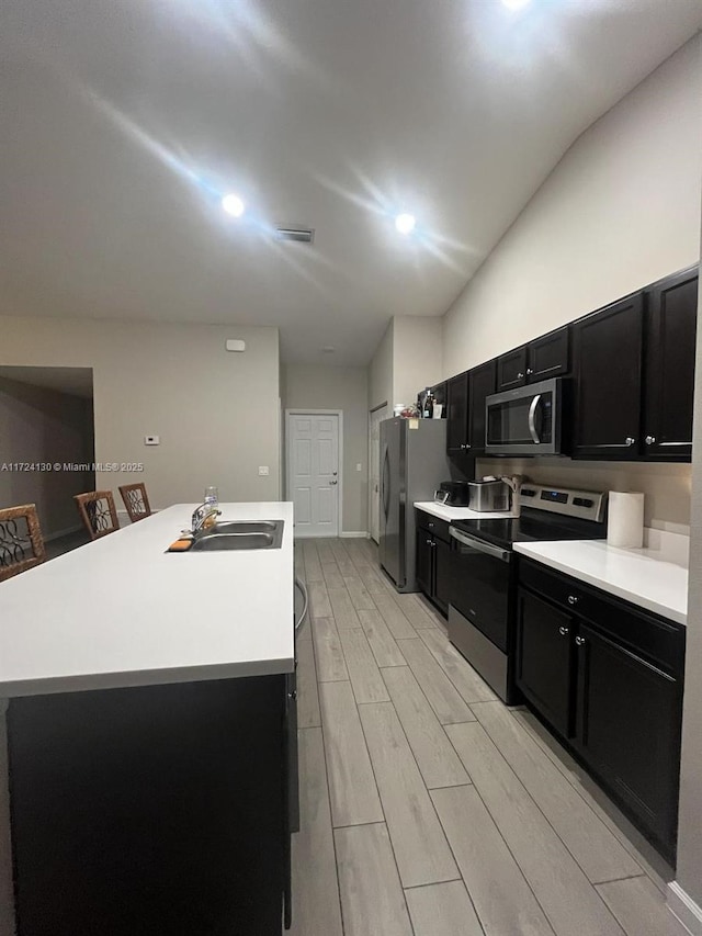 kitchen with sink, light hardwood / wood-style flooring, an island with sink, and appliances with stainless steel finishes