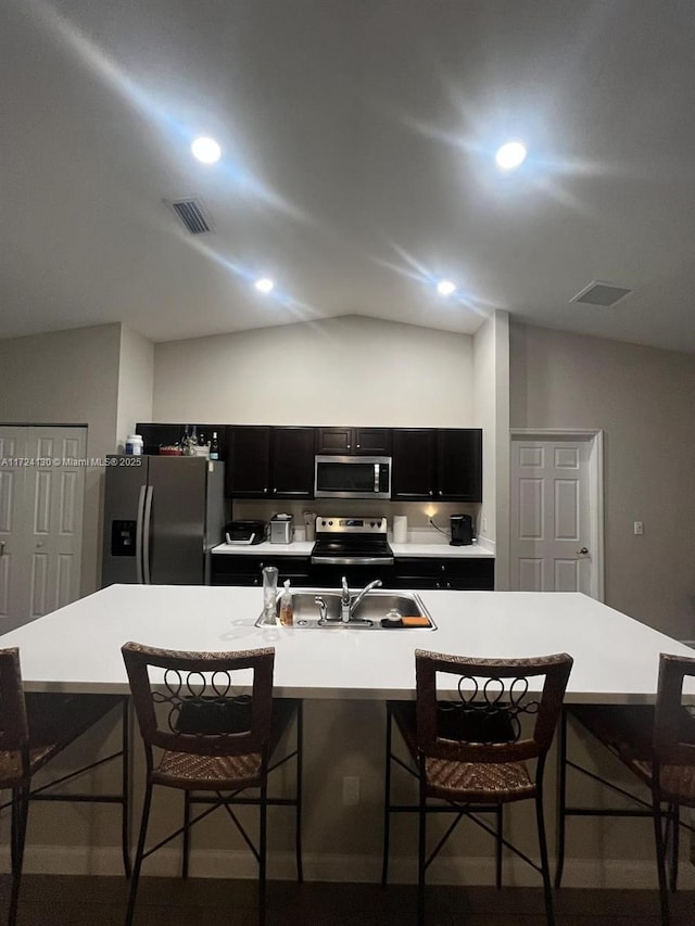 kitchen featuring lofted ceiling, appliances with stainless steel finishes, a kitchen breakfast bar, and an island with sink