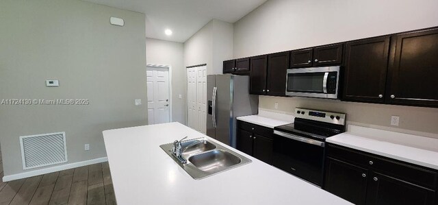 kitchen featuring appliances with stainless steel finishes, a sink, dark wood-style flooring, baseboards, and light countertops