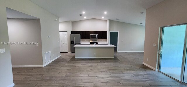 kitchen with stainless steel appliances, high vaulted ceiling, a kitchen island with sink, wood finished floors, and light countertops