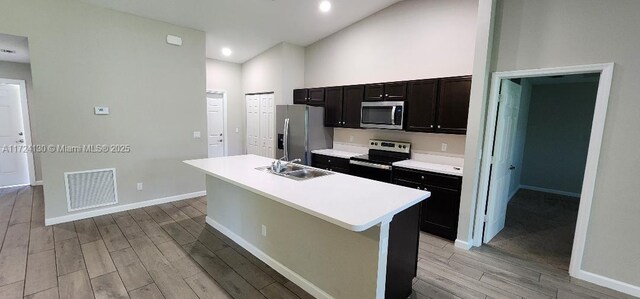 kitchen with stainless steel appliances, a sink, light wood finished floors, light countertops, and a kitchen island with sink