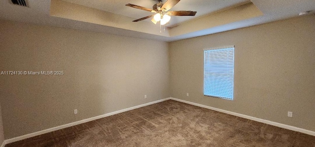 empty room featuring a ceiling fan, a raised ceiling, baseboards, and dark carpet