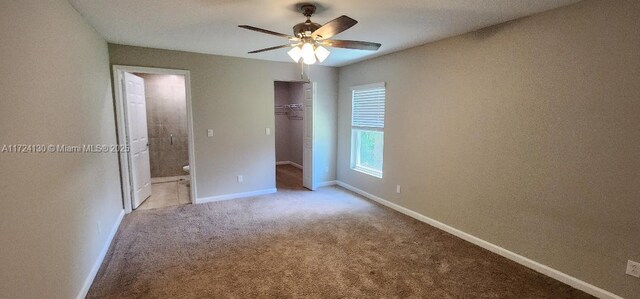 unfurnished bedroom featuring light colored carpet, connected bathroom, baseboards, a closet, and ceiling fan