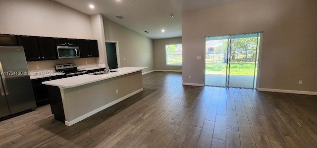 kitchen featuring appliances with stainless steel finishes, dark cabinetry, open floor plan, dark wood-style flooring, and light countertops