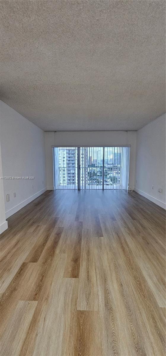 empty room with light wood-type flooring and a textured ceiling