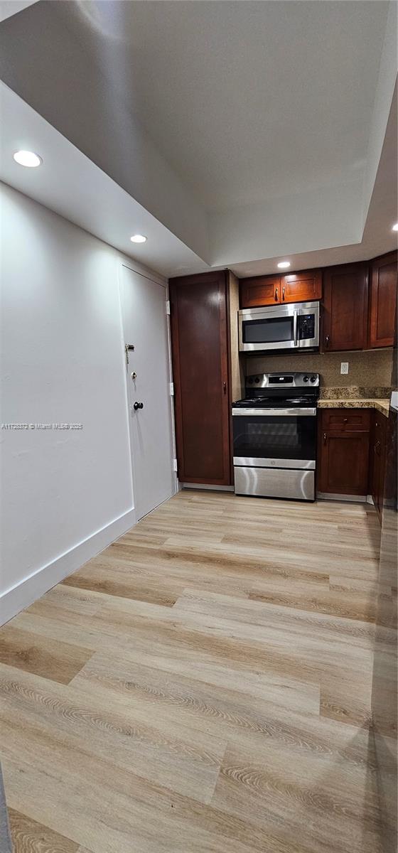 kitchen featuring backsplash, dark brown cabinetry, light stone counters, stainless steel appliances, and light hardwood / wood-style flooring