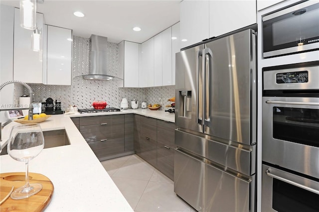 kitchen with white cabinets, decorative light fixtures, wall chimney exhaust hood, and appliances with stainless steel finishes