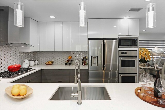 kitchen with wall chimney range hood, hanging light fixtures, white cabinets, and appliances with stainless steel finishes