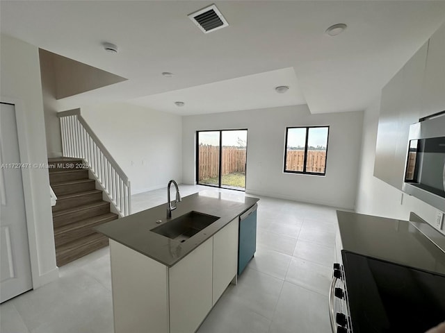 kitchen with appliances with stainless steel finishes, white cabinetry, sink, light tile patterned floors, and a center island with sink