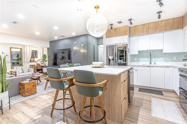 kitchen featuring pendant lighting, decorative backsplash, sink, white cabinetry, and light hardwood / wood-style flooring