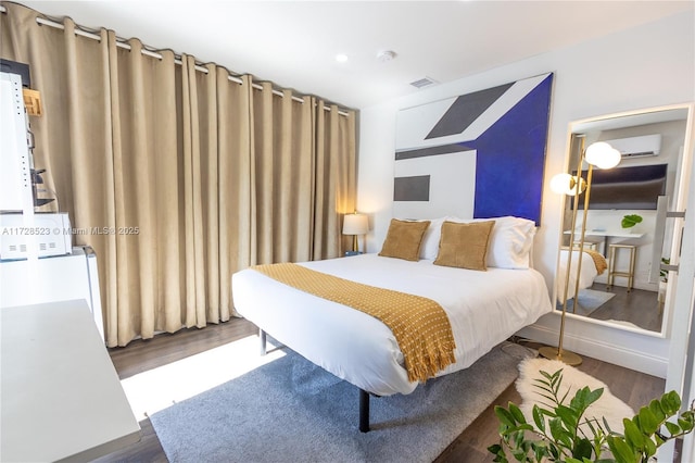 bedroom with dark hardwood / wood-style flooring and a wall mounted AC