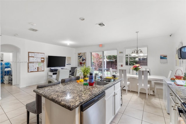 kitchen with stainless steel dishwasher, white cabinets, light stone counters, and an island with sink