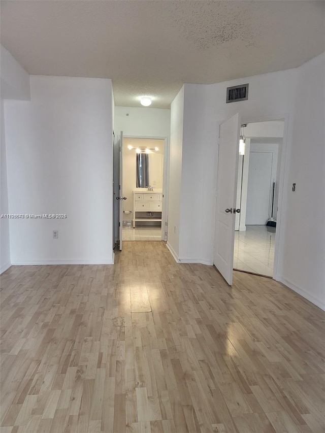 unfurnished room with a textured ceiling and light wood-type flooring