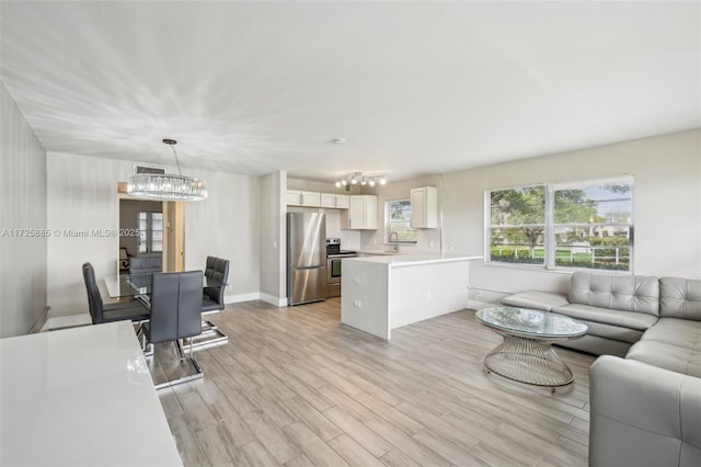 living room with an inviting chandelier, sink, and light wood-type flooring