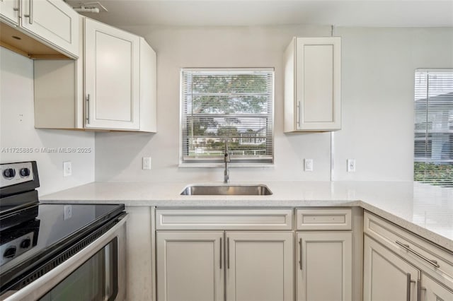 kitchen featuring white cabinetry, sink, stainless steel range with electric cooktop, and light stone countertops