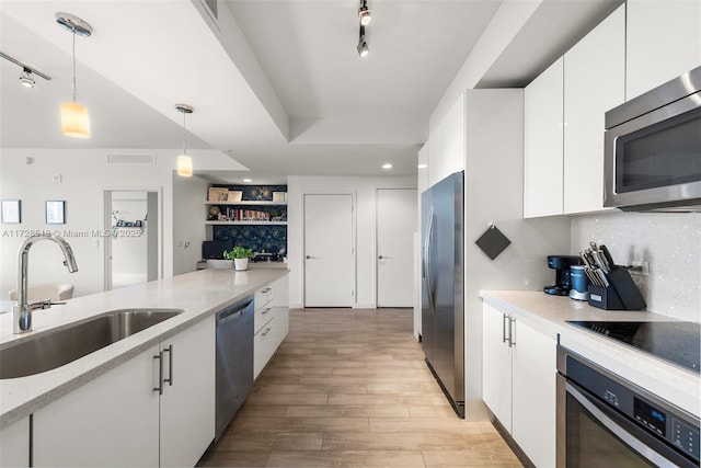 kitchen with white cabinets, stainless steel appliances, sink, hanging light fixtures, and light hardwood / wood-style flooring