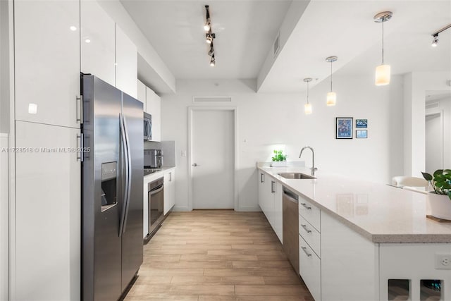 kitchen featuring pendant lighting, sink, backsplash, white cabinetry, and stainless steel appliances