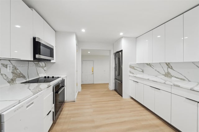 kitchen featuring light stone countertops, white cabinetry, tasteful backsplash, and black appliances