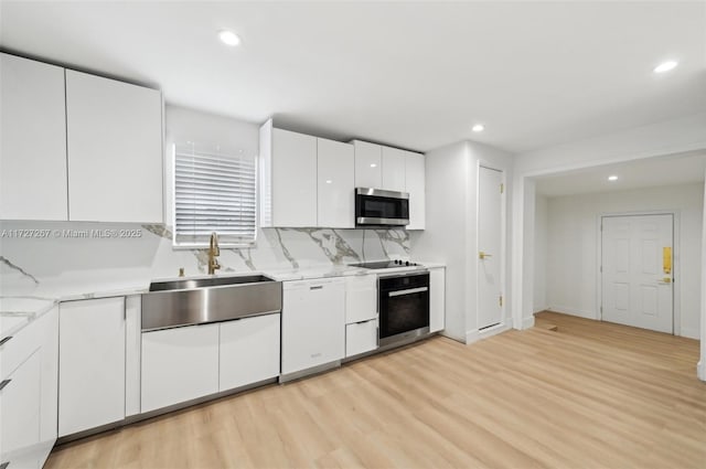 kitchen with oven, white dishwasher, white cabinetry, light hardwood / wood-style flooring, and light stone countertops