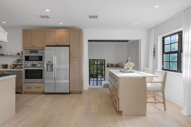 kitchen with a kitchen island, light hardwood / wood-style floors, appliances with stainless steel finishes, a kitchen breakfast bar, and light brown cabinetry