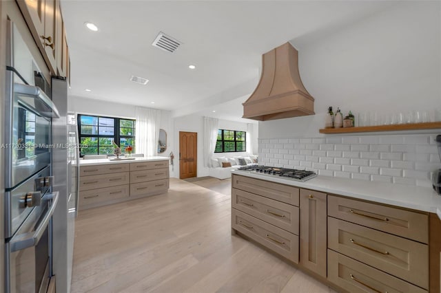 kitchen featuring premium range hood, a wealth of natural light, light hardwood / wood-style floors, and tasteful backsplash