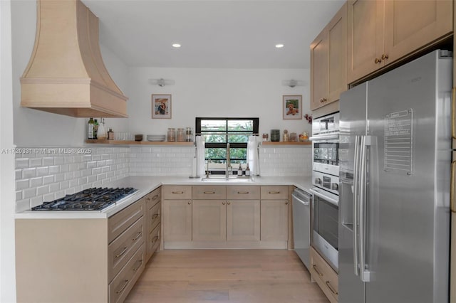 kitchen featuring light brown cabinetry, premium range hood, decorative backsplash, and appliances with stainless steel finishes