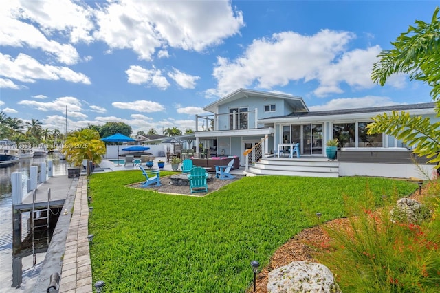 back of house featuring an outdoor living space with a fire pit, a balcony, a yard, a water view, and a patio