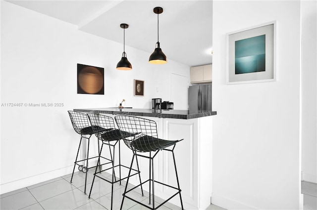 kitchen featuring light tile patterned floors, stainless steel fridge, a breakfast bar area, hanging light fixtures, and white cabinets