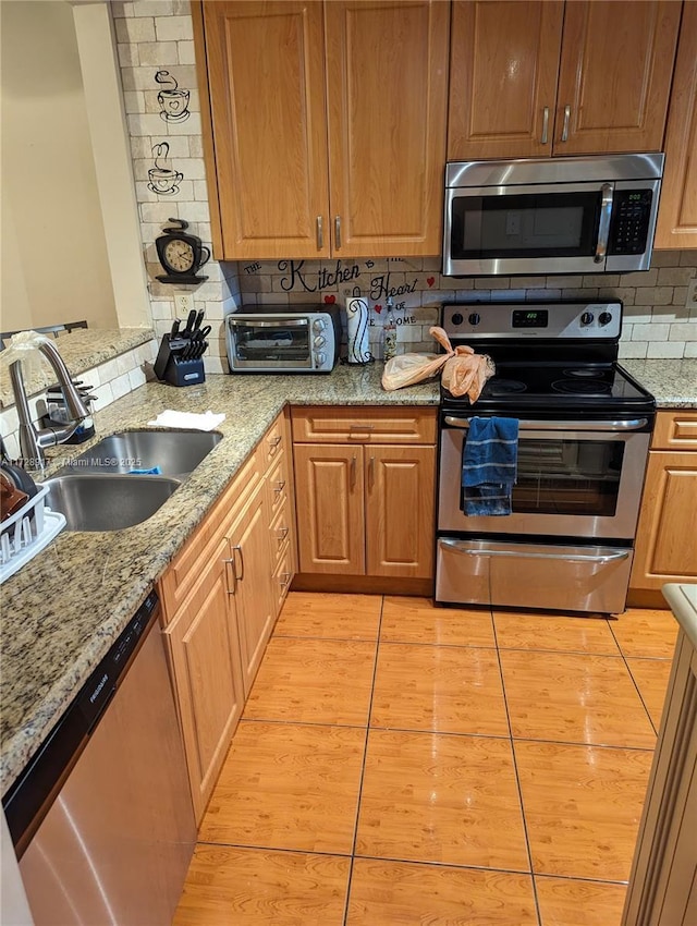 kitchen with tasteful backsplash, appliances with stainless steel finishes, sink, and light stone counters