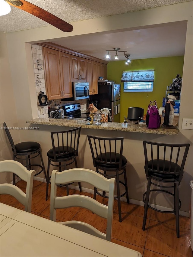 kitchen with a textured ceiling, stainless steel appliances, kitchen peninsula, and a breakfast bar