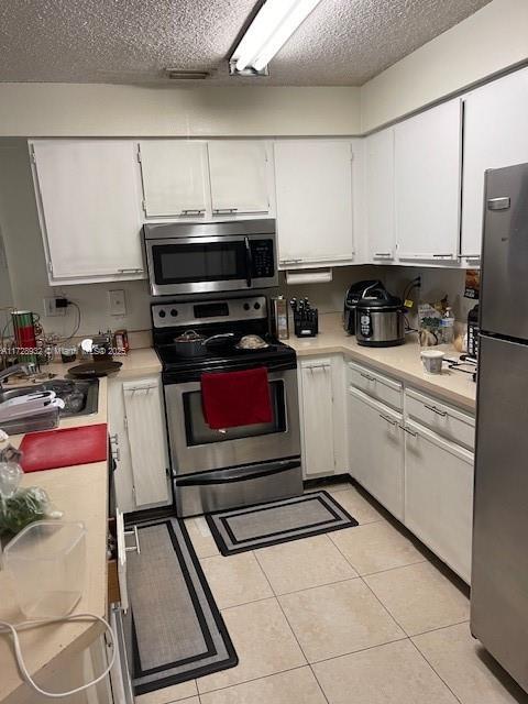 kitchen with light tile patterned floors, a textured ceiling, white cabinets, and stainless steel appliances