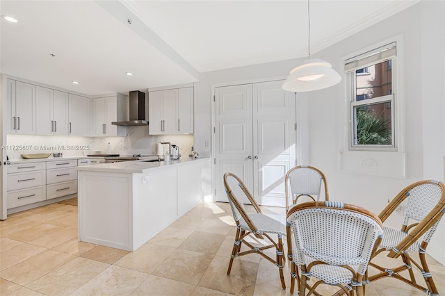 kitchen with white cabinets, decorative light fixtures, wall chimney range hood, tasteful backsplash, and kitchen peninsula