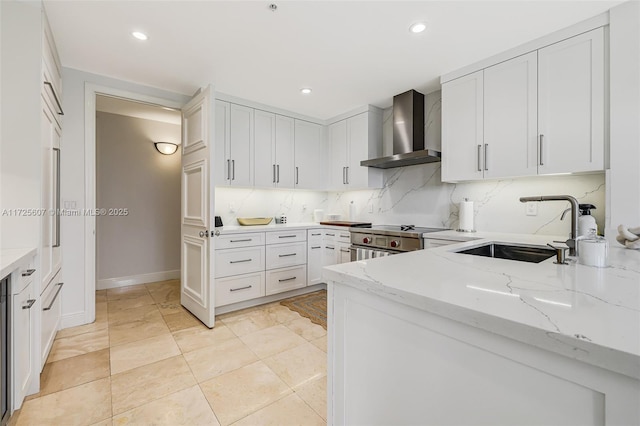 kitchen featuring high end stainless steel range, wall chimney range hood, white cabinetry, sink, and backsplash