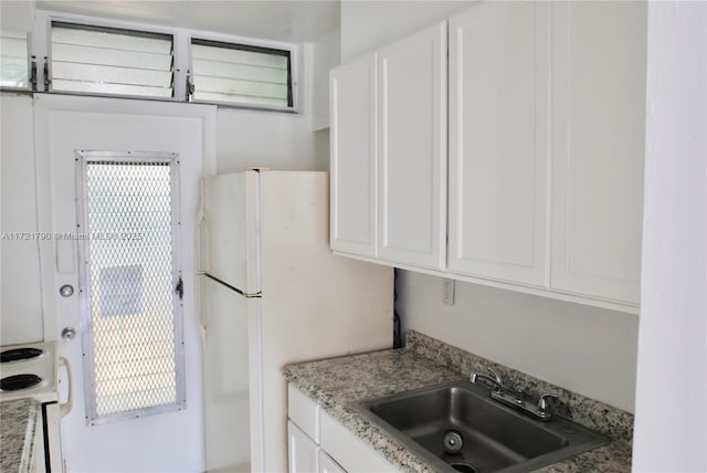 kitchen with light stone countertops, sink, white cabinetry, and white fridge