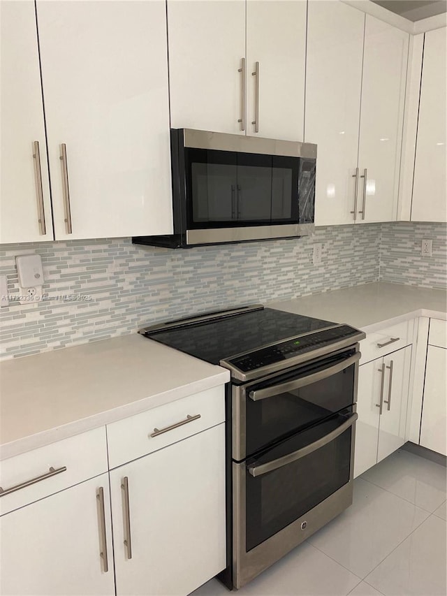 kitchen featuring light tile patterned floors, stainless steel appliances, decorative backsplash, and white cabinets