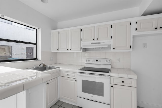 kitchen with light tile patterned floors, tile countertops, white cabinetry, white range with electric cooktop, and sink