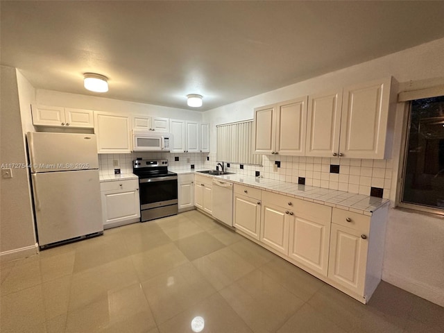 kitchen with light tile patterned floors, tasteful backsplash, white appliances, white cabinets, and sink