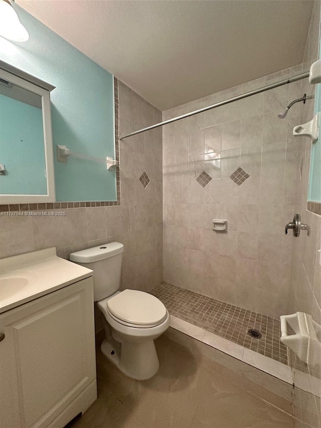 bathroom featuring toilet, vanity, tile walls, tile patterned floors, and tiled shower