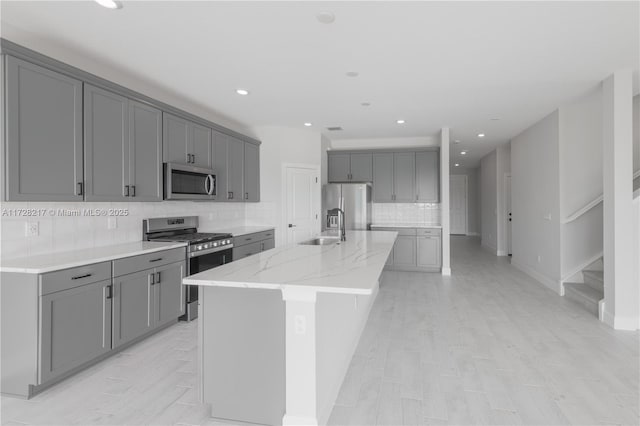 kitchen featuring appliances with stainless steel finishes, an island with sink, a sink, and gray cabinetry