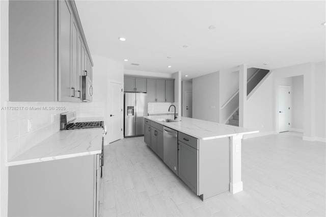 kitchen featuring stainless steel appliances, a sink, gray cabinets, light stone countertops, and tasteful backsplash