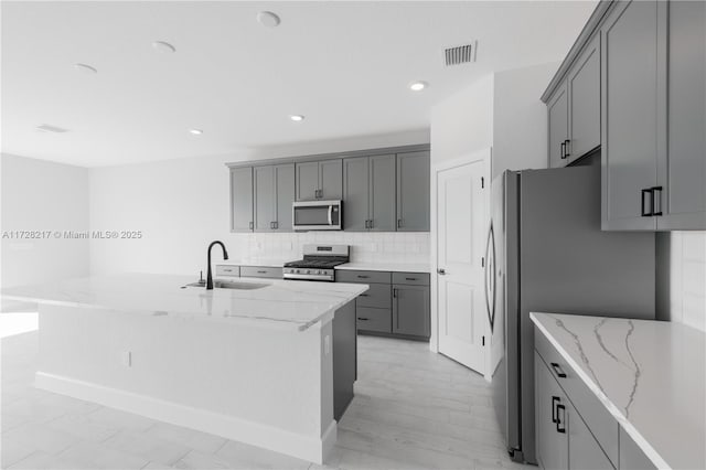 kitchen featuring light stone counters, stainless steel appliances, gray cabinets, visible vents, and a sink