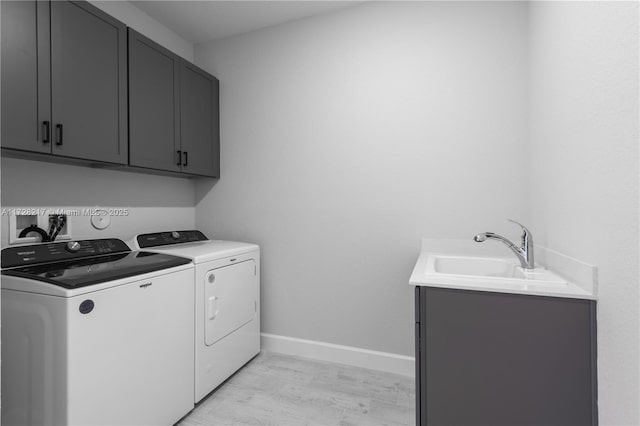 laundry area with light wood finished floors, cabinet space, washing machine and dryer, a sink, and baseboards