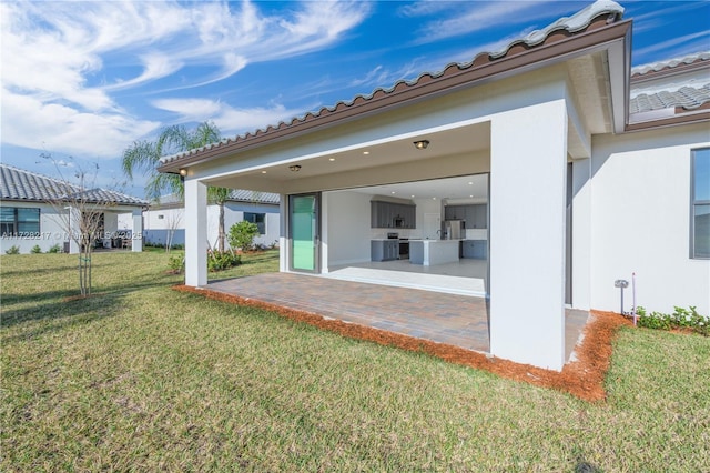 rear view of house featuring a garage, a lawn, a patio, a tile roof, and stucco siding