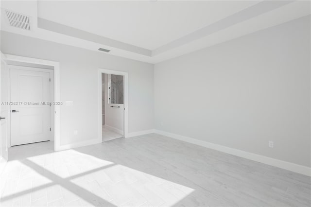 unfurnished bedroom with light wood-type flooring, a tray ceiling, visible vents, and baseboards