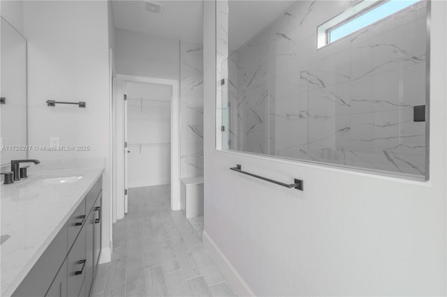 bathroom with a walk in closet, visible vents, vanity, and a marble finish shower