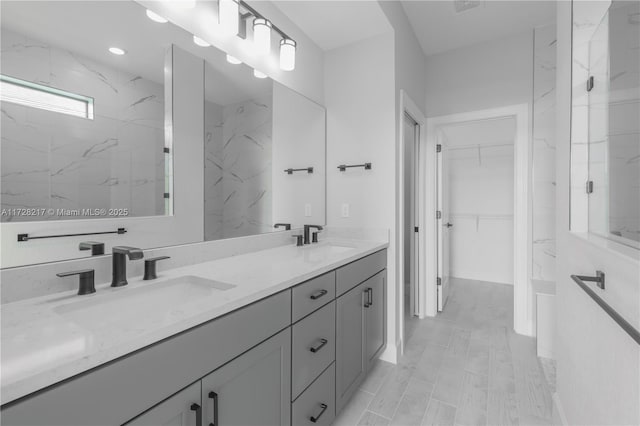 bathroom with a spacious closet, double vanity, a sink, and a marble finish shower